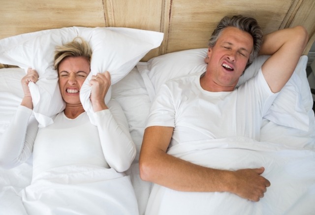 Frustrated woman sleeping next to snoring man in need of sleep apnea therapy
