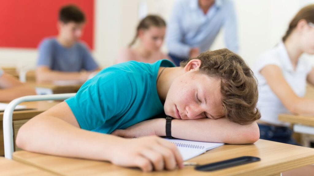 A teenage boy sleeping at his desk during class.