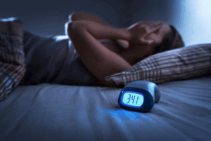 Woman unable to sleep lying next to a clock that shows the early morning hour