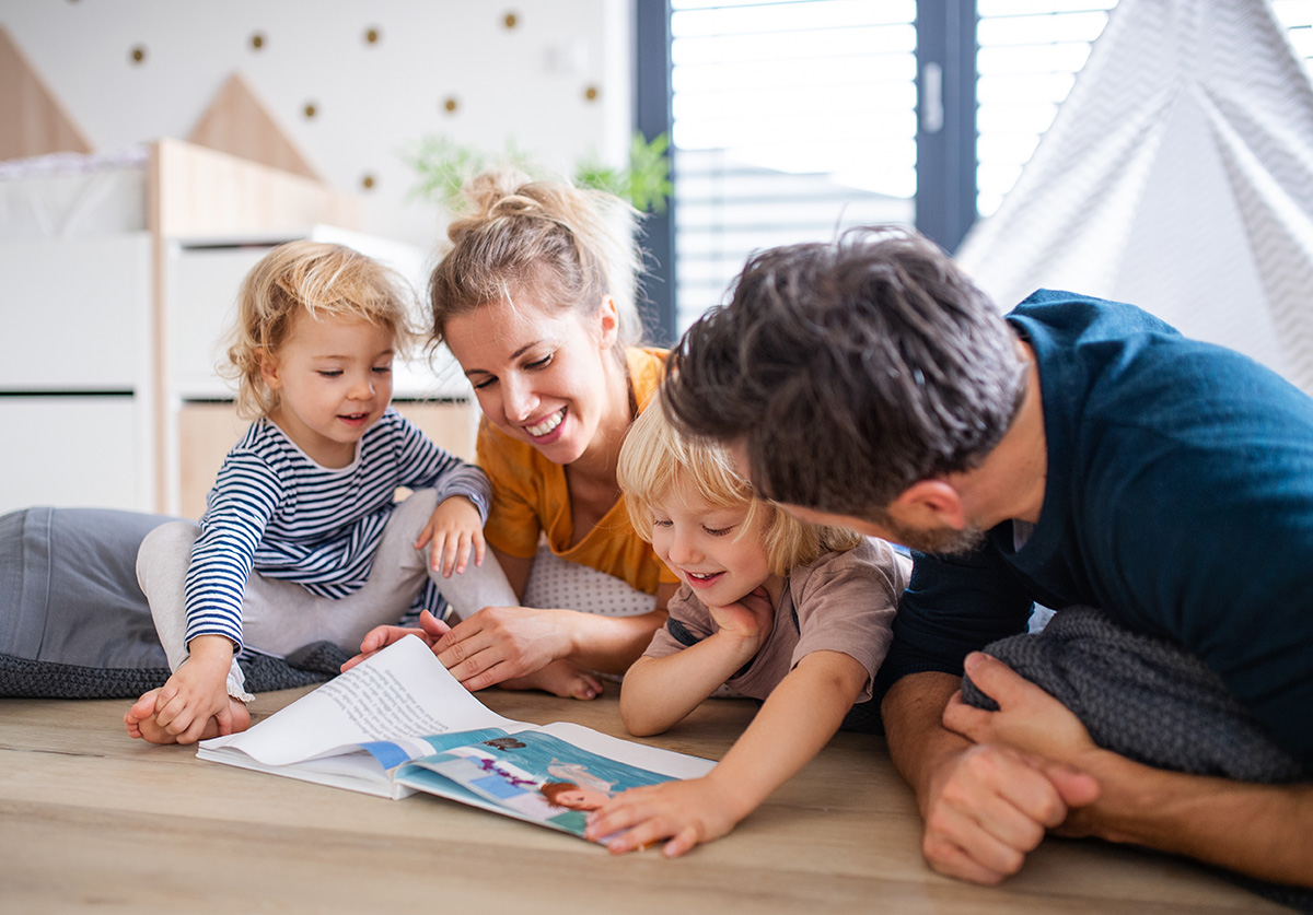 Two parents reading a picture book with their toddlers on the floor at home