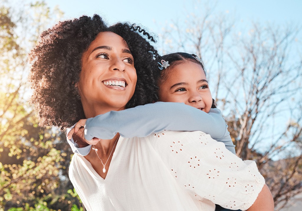 Smiling mother carrying her young daughter on her back outdoors